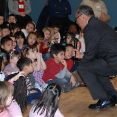 This is a colour photograph of Steven Point kneeling down to speak with a group of elementary school students in 2011.