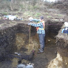 This is a photograph of an archaeologist standing in an excavation of a house.