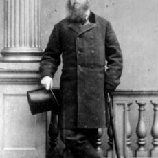 This is a black and white photograph of Joseph Trutch, standing, holding a top hat in one hand.