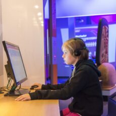 This is a photograph showing the profile of a child with headphones on sitting at a computer kiosk at the Our Living Languages exhibition.