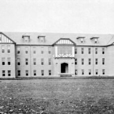 A black and white photograph of the exterior of the Coqualeetza Residential School. It is a large four-storey building located in a vast clearing.