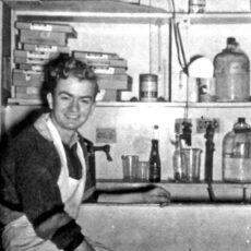 Stanley Fox seated wearing an apron in a photography darkroom.