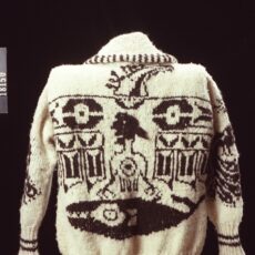 A photograph of the back of a white knitted sweater with dark brown designs depicting a thunderbird and whale.