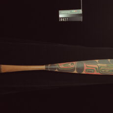 A photograph of a long-bladed canoe paddle with colourful Heiltsuk designs on its blade.