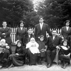 A black and white photograph that shows a large First Nations family, formally dressed, outside in a garden with their dog.