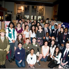 A posed photograph of about 35 Heritage Fair students with adults. Heritage Fair projects are in the background.