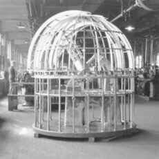Scale model of the Plaskett Telescope in a dome (without outer covering). Factory workers and various equipment in the background.