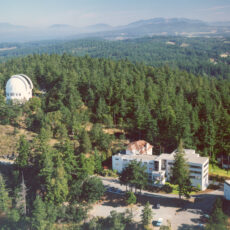 Aerial view of the DAO complex including several office buildings and the observatory, surrounded by evergreen trees.