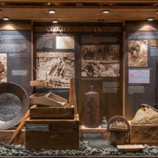 A display case full of gold-panning tools such as rakes and a dented metal pan.