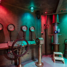 Medal walls of a replica submarine with a steering wheel, pressure dials, and periscope.