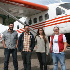 Four people standing in front of a small propeller plane.