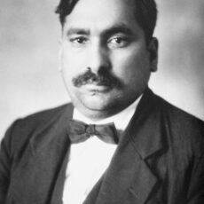 A black and white head-and-shoulders portrait photograph of a man. He is wearing a dark suit with a bowtie and sports neatly combed hair and a moustache.